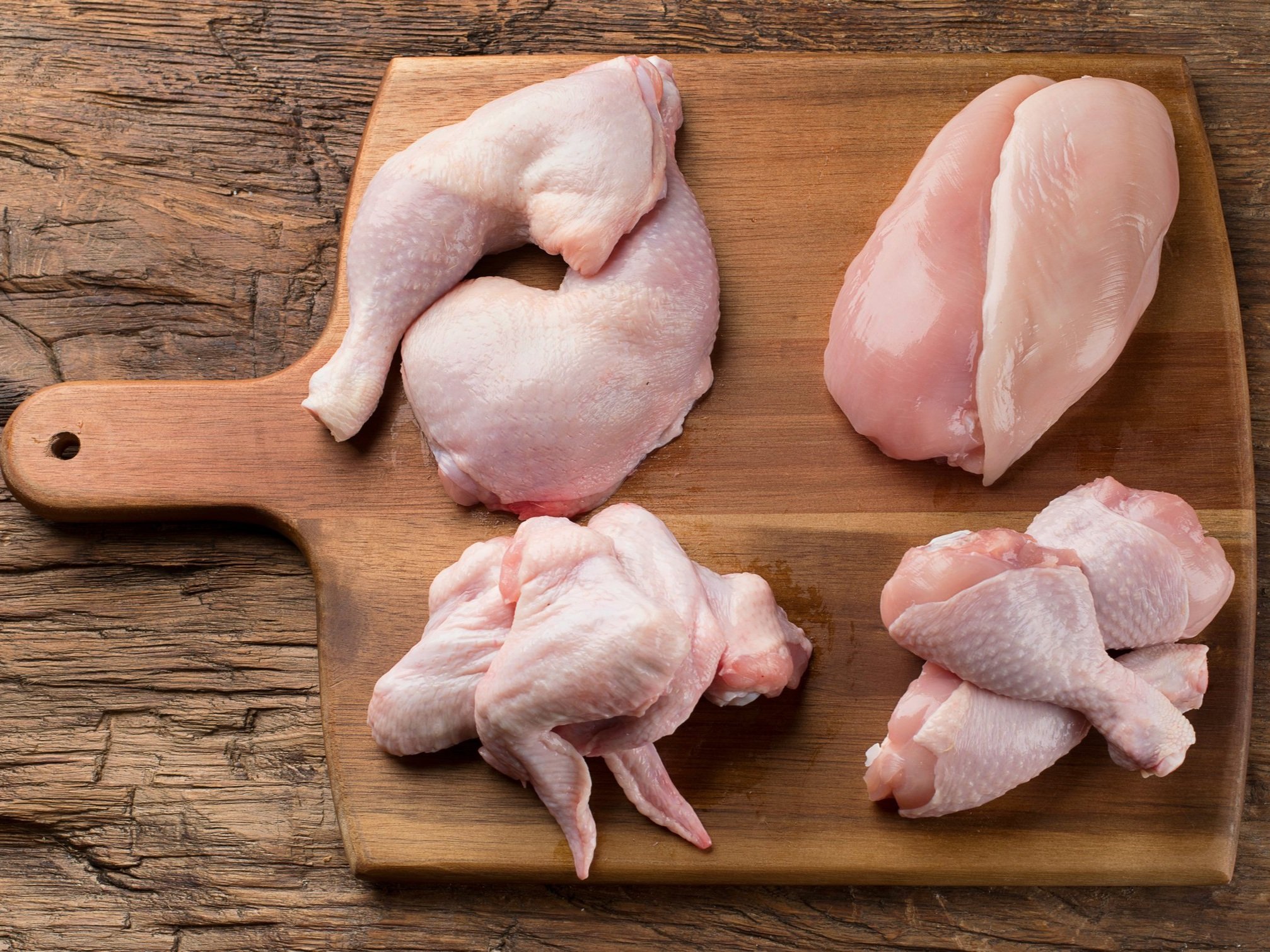 chicken_cuts_variety_woodcuttingboard (1) Raw chicken pieces displayed on a wooden cutting board, including chicken thighs, breasts, and drumsticks, ideal for meal preparation and cooking.